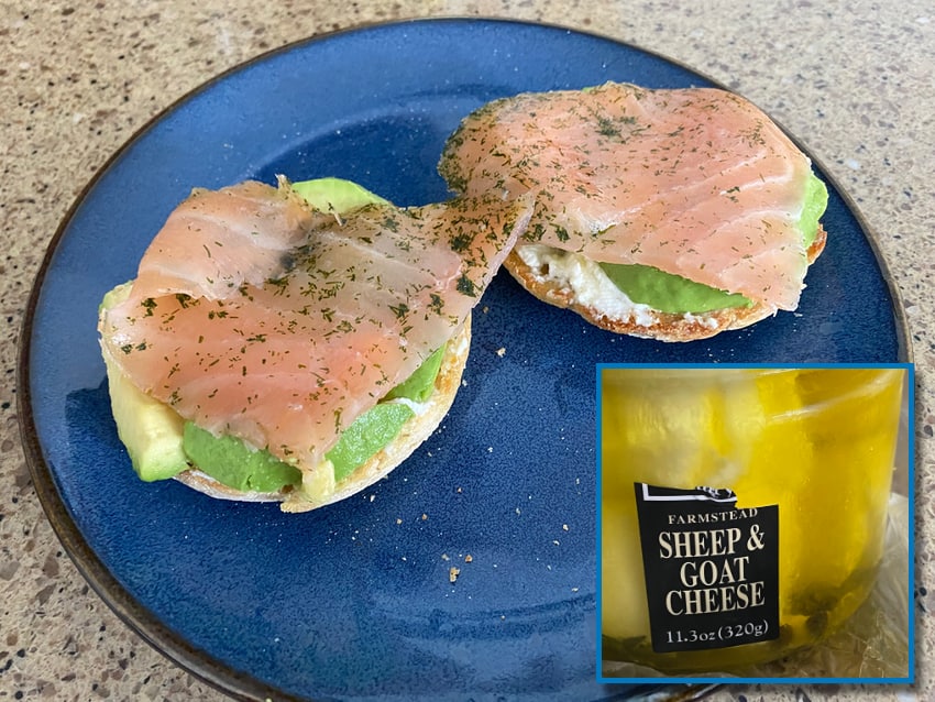 a breakfast sandwich with sheep & goat cheese, avocado, and smoked salmon on an english muffin.
